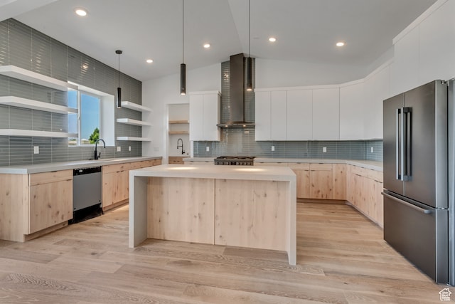 kitchen featuring lofted ceiling, wall chimney exhaust hood, light hardwood / wood-style flooring, appliances with stainless steel finishes, and a center island