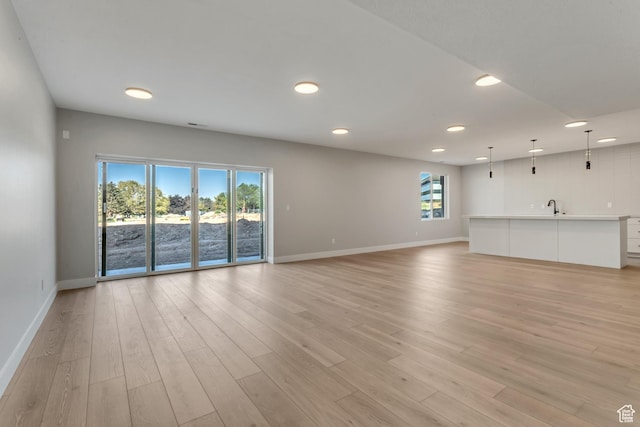 unfurnished living room with a sink, light wood finished floors, baseboards, and recessed lighting
