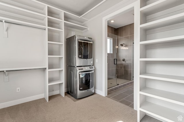 laundry area with stacked washer / drying machine, laundry area, carpet floors, tile patterned flooring, and baseboards