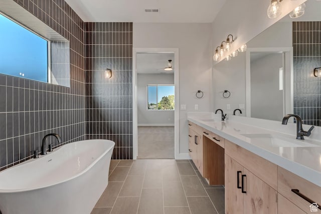 full bath featuring a soaking tub, tile walls, ceiling fan, and a sink