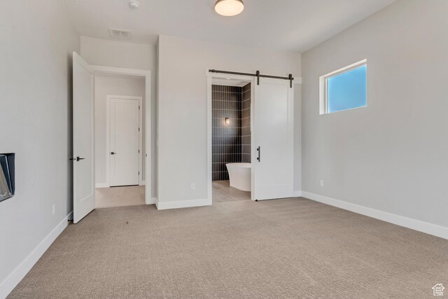 unfurnished bedroom with light colored carpet, a barn door, baseboards, and visible vents