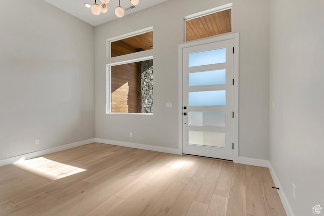 doorway with light wood-style flooring, a notable chandelier, baseboards, and visible vents