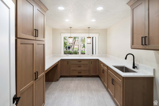 kitchen with a textured ceiling, kitchen peninsula, decorative light fixtures, and sink