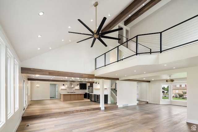 unfurnished living room with beam ceiling, light hardwood / wood-style flooring, and high vaulted ceiling