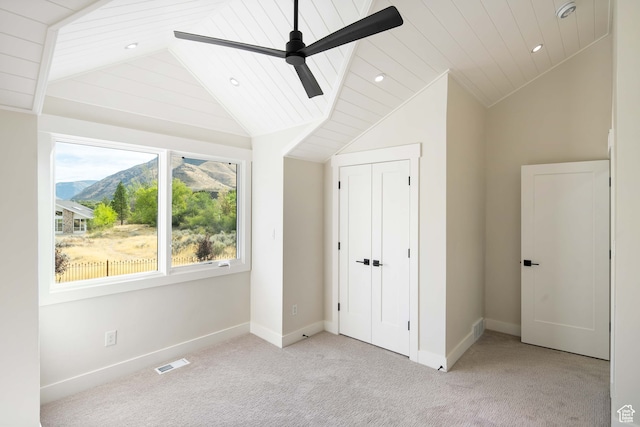 unfurnished bedroom with a mountain view, ceiling fan, light colored carpet, and vaulted ceiling