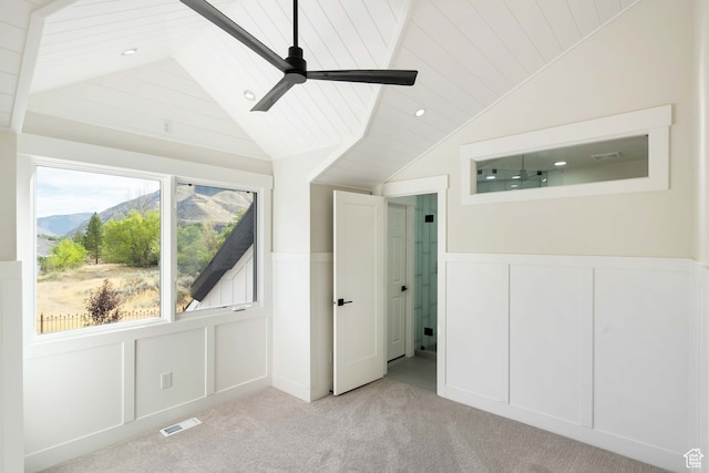 unfurnished bedroom featuring ceiling fan, light colored carpet, vaulted ceiling, and a mountain view