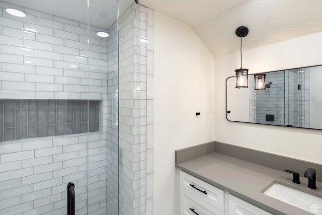 bathroom with vanity, lofted ceiling, a tile shower, and a textured ceiling