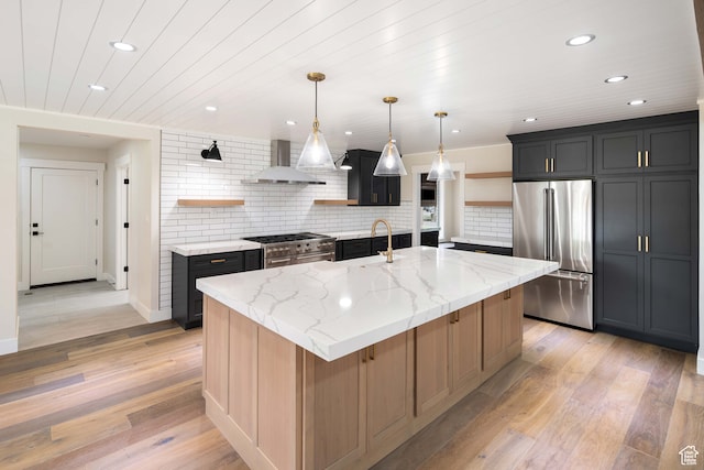 kitchen featuring light wood-type flooring, light stone counters, high end appliances, wall chimney exhaust hood, and a center island with sink
