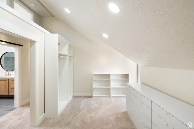 spacious closet featuring light colored carpet, sink, and vaulted ceiling