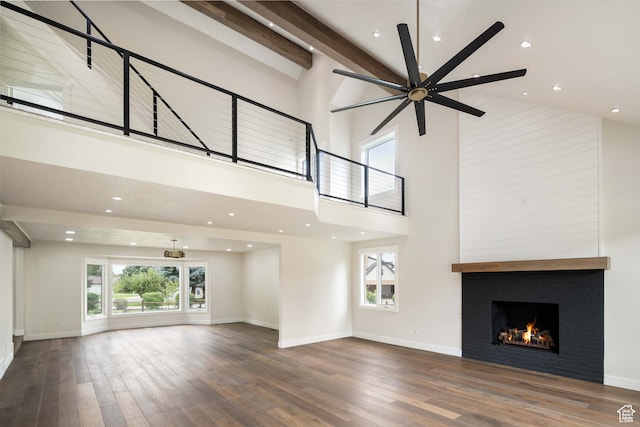 unfurnished living room featuring ceiling fan, beamed ceiling, high vaulted ceiling, a large fireplace, and hardwood / wood-style floors