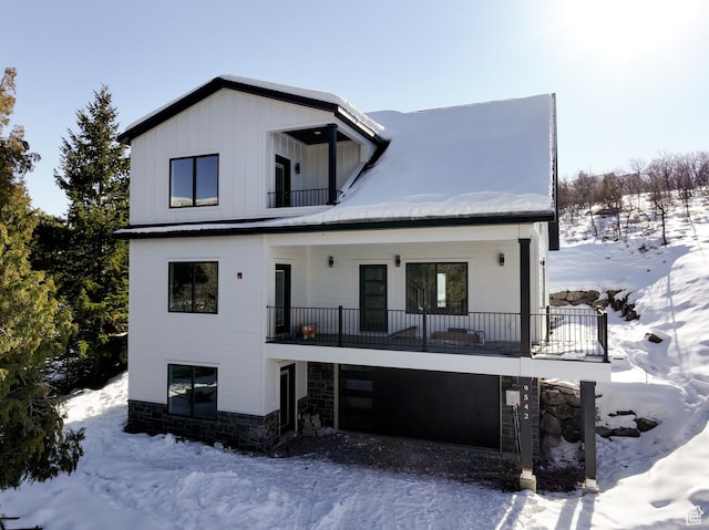 snow covered back of property with a balcony and a garage