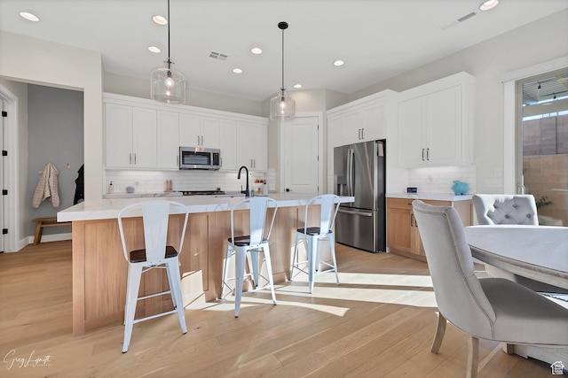 4755 S Purcell Dr, St George, UT 84790 - kitchen with light countertops, light wood finished floors, visible vents, a kitchen island with sink, and appliances with stainless steel finishes