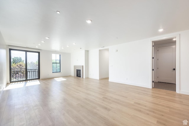unfurnished living room with a glass covered fireplace, recessed lighting, baseboards, and light wood-style floors