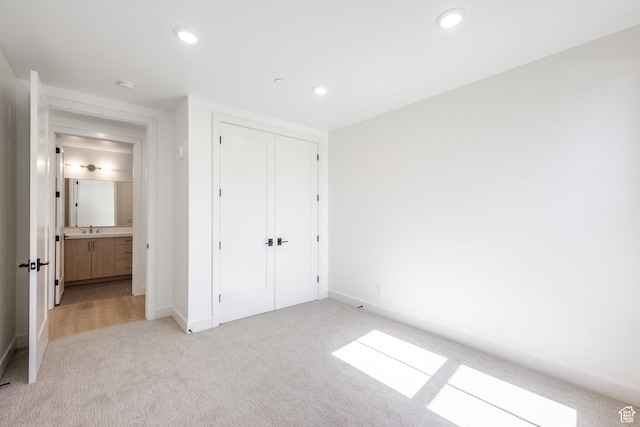unfurnished bedroom with baseboards, recessed lighting, a sink, a closet, and light colored carpet