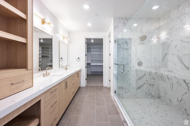 full bath with a marble finish shower, a spacious closet, double vanity, and a sink