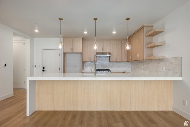 kitchen with under cabinet range hood, light wood-type flooring, a peninsula, and light countertops