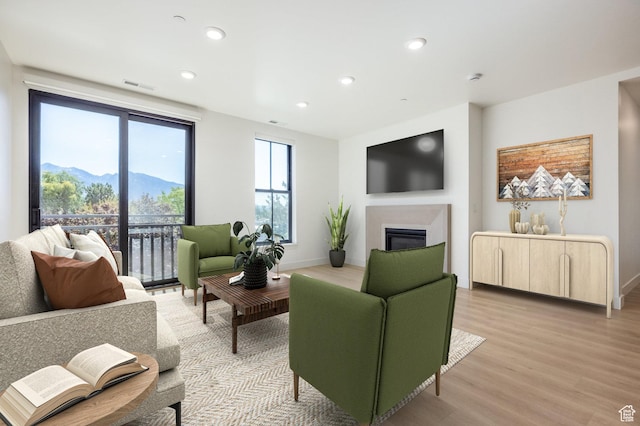 living room with light wood finished floors, visible vents, baseboards, recessed lighting, and a glass covered fireplace