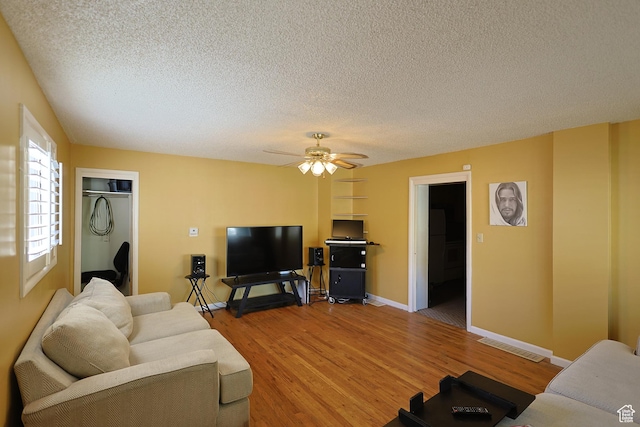 living room featuring a textured ceiling, light wood-style flooring, ceiling fan, and baseboards