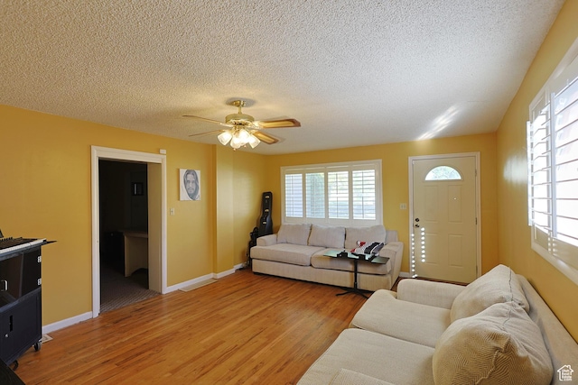 living area featuring light wood-style flooring, plenty of natural light, a ceiling fan, a textured ceiling, and baseboards