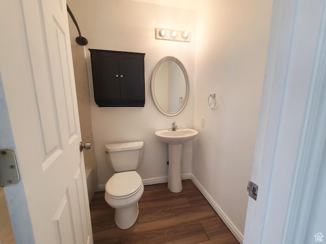 half bath with a sink, toilet, wood finished floors, and baseboards