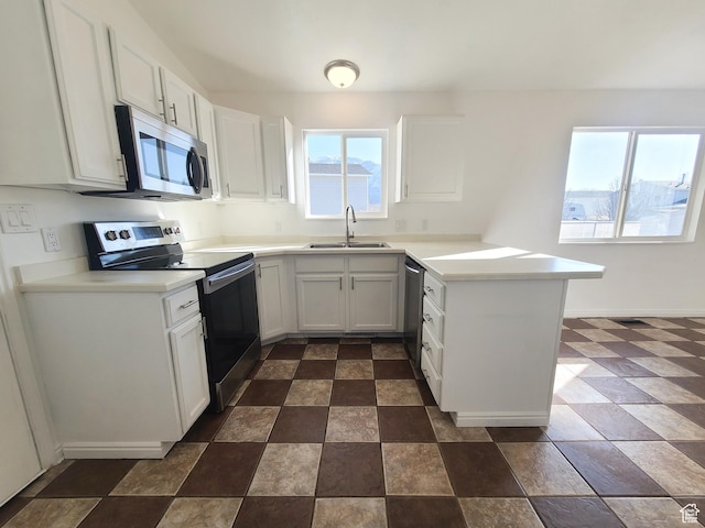 kitchen with a peninsula, white cabinetry, stainless steel appliances, and a sink