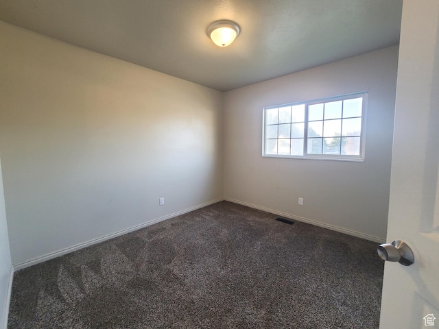 unfurnished room with baseboards, dark colored carpet, and visible vents