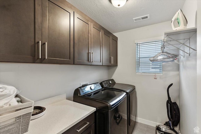 clothes washing area featuring separate washer and dryer, baseboards, a textured ceiling, visible vents, and cabinet space