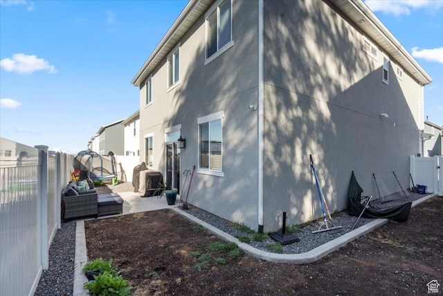 view of property exterior with a trampoline, a patio area, a fenced backyard, and stucco siding