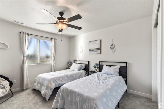 carpeted bedroom with a textured ceiling, baseboards, a ceiling fan, and visible vents