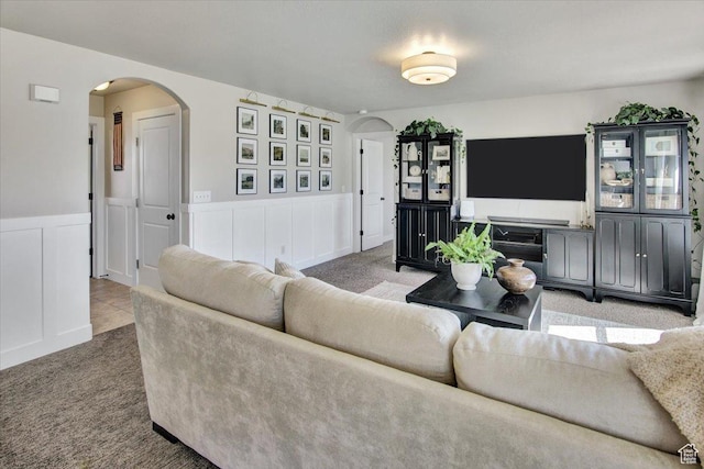 carpeted living area with a wainscoted wall and arched walkways