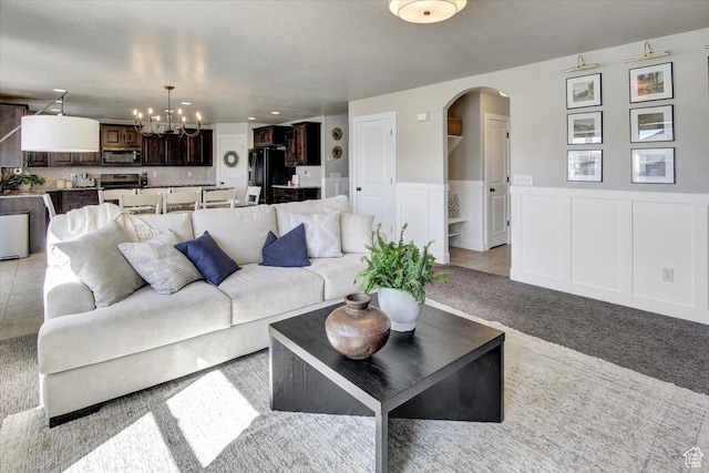 living area featuring a decorative wall, a chandelier, arched walkways, light carpet, and a wainscoted wall