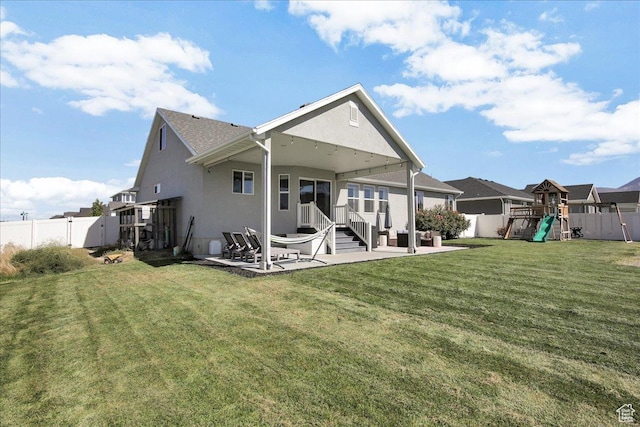 rear view of house with a playground, a fenced backyard, a yard, a patio, and stucco siding