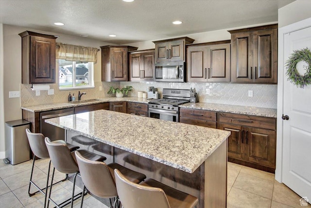 kitchen featuring a sink, a breakfast bar area, appliances with stainless steel finishes, light stone countertops, and a kitchen island