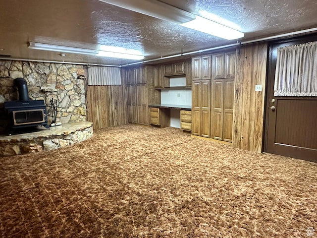 finished basement featuring a textured ceiling, wood walls, and a wood stove