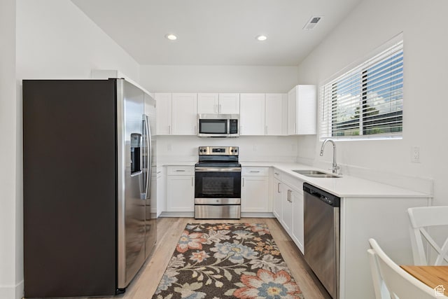 kitchen with white cabinetry, a sink, light countertops, stainless steel appliances, and light wood-style flooring