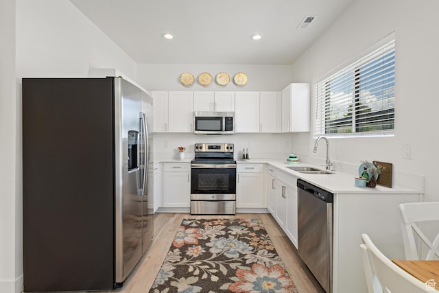 kitchen with white cabinets, appliances with stainless steel finishes, a sink, light wood-style flooring, and visible vents