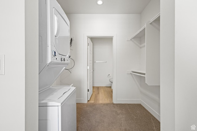 clothes washing area featuring laundry area, light colored carpet, baseboards, stacked washer and clothes dryer, and recessed lighting