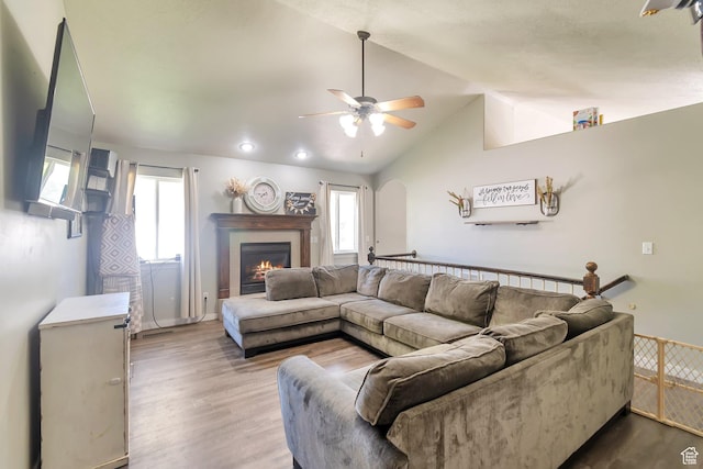 living room with a ceiling fan, wood finished floors, vaulted ceiling, and a lit fireplace