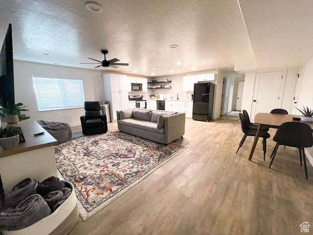 living room with a textured ceiling, ceiling fan, baseboards, and light wood-style floors