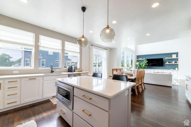 kitchen featuring a sink, a textured ceiling, stainless steel microwave, and dark wood finished floors