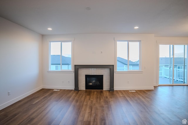 unfurnished living room with visible vents, dark wood-style flooring, baseboards, a glass covered fireplace, and recessed lighting