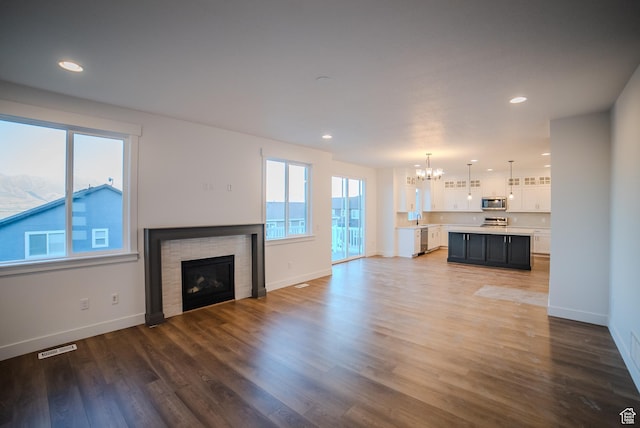 unfurnished living room with baseboards, a fireplace, a chandelier, and wood finished floors