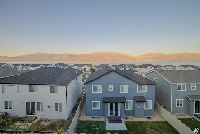 back of house at dusk with a mountain view, a residential view, stucco siding, a fenced backyard, and a lawn