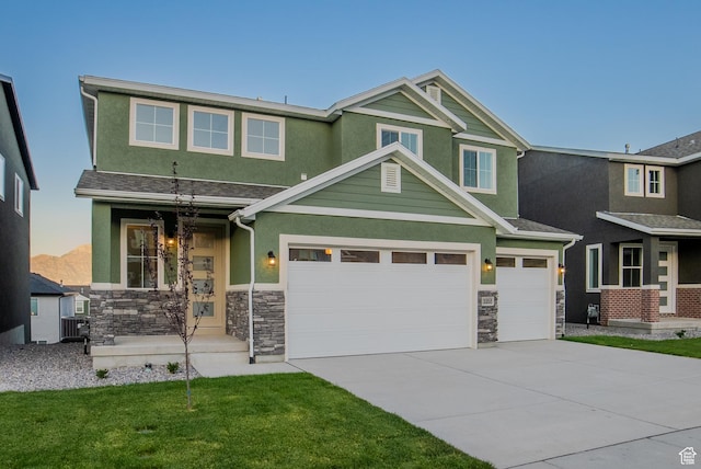 craftsman-style home with a garage, stucco siding, concrete driveway, stone siding, and a front lawn