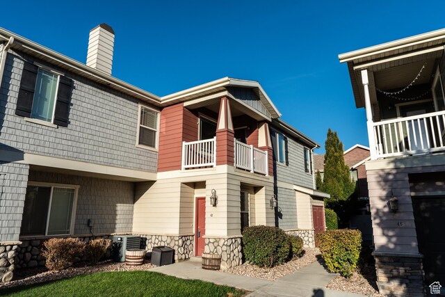 view of front facade with a chimney, cooling unit, stone siding, and a balcony