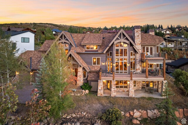 75 Hidden Oaks Ln, Park City, UT 84060 - back of property at dusk with a chimney, a balcony, a patio, and stone siding