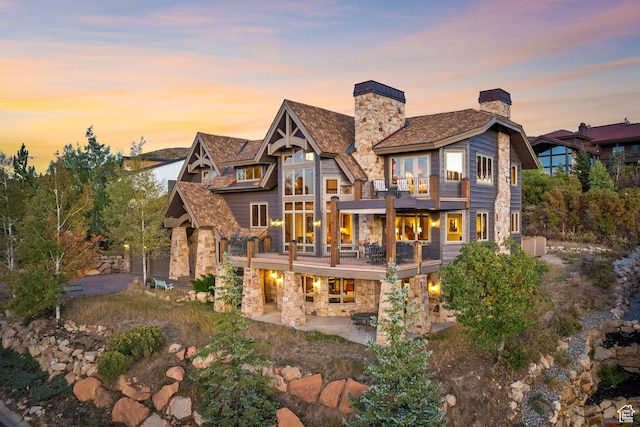75 Hidden Oaks Ln, Park City, UT 84060 - back of house at dusk featuring a patio, a chimney, stone siding, and a balcony
