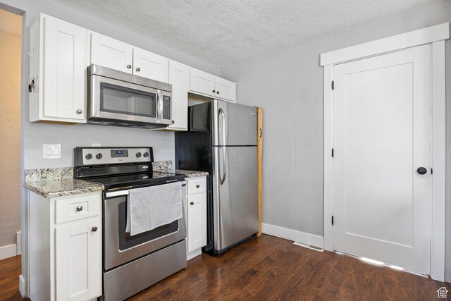 kitchen featuring dark wood-style floors, light stone counters, stainless steel appliances, and baseboards