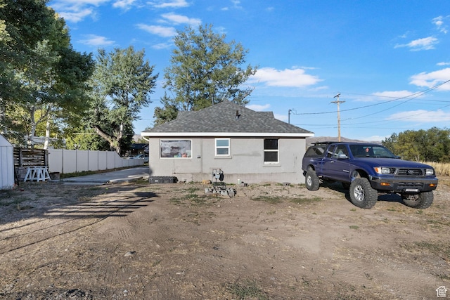 exterior space featuring roof with shingles, stucco siding, and fence