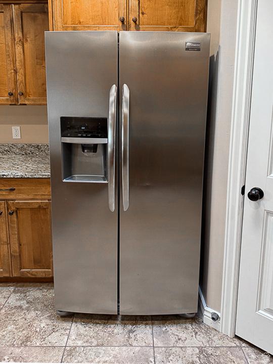 kitchen with brown cabinets, light stone countertops, and stainless steel fridge